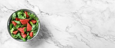 Feta peynirli taze karpuz salatası, roka, ıspanak ve açık mermer arka planda peçeteli yeşiller. Sağlıklı yemek, temiz yemek, Buda kasesi salatası, detoks, üst manzara.