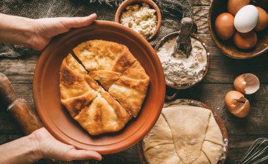 Düz ekmek tutan eller ya da süzme peynirli yuvarlak turtalar, yumurtalar, kırsal ahşap arka planda tabakta bitki. Ev yapımı pişirme, sağlıklı gıda konsepti, üst görünüm, tonlama