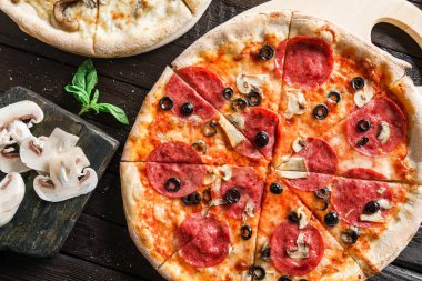 Prosciutto, sosis, jambon, peynirli parmesan peyniri, domates, mantar, koyu ahşap arka planda zeytinli pizza. Piknik şirketi için fast food öğle yemeği.