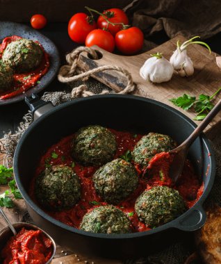 Vejetaryen ıspanak topları, tavada nohut, domates sosu, soğan, arka planda maydanoz, ahşap masa üzerinde peçete. Sağlıklı yemek, temiz yemek, vejetaryen diyeti, yakın çekim.