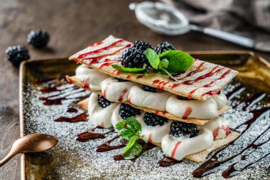 Böğürtlenli ve kremalı yaz tatlısı, ahşap masadaki nane şekeriyle süslenmiş. Lezzetli tatlı ve çikolata, yakın çekim.