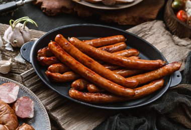 Tavada kızartılmış sosis, ahşap zemin üzerinde sarımsak ve baharat. Et aperatifi, kapat.