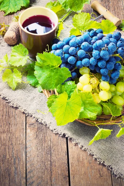 Vino tinto y uvas en ambiente vintage con corchos sobre mesa de madera — Foto de Stock