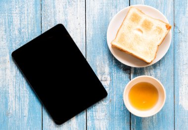 Siyah ekran Tablet, tost, tatlım mavi ahşap zemin üzerinde.