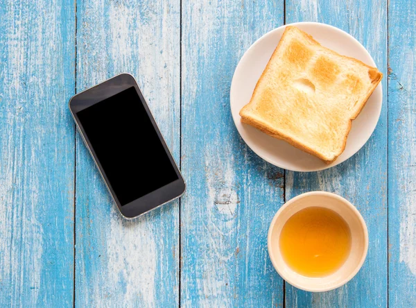 Siyah ekran akıllı telefon, tost, mavi ahşap zemin üzerinde tatlım.
