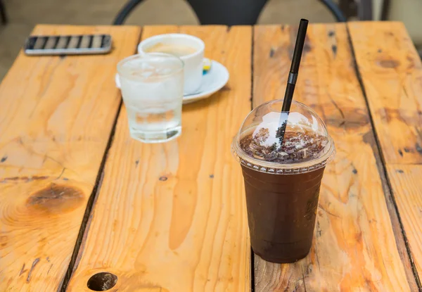 Eiskaffee in Kunststoffglas, Kaffeetasse, Glaswasser auf Holz — Stockfoto