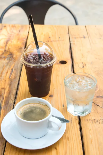 Холодный кофе в пластиковом стекле, чашка кофе, стеклянная вода на дереве — стоковое фото
