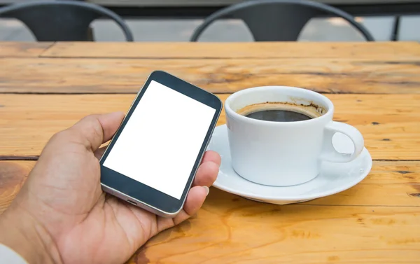 Vit skärm smart telefon i handen, vit kaffekopp på trä flo — Stockfoto