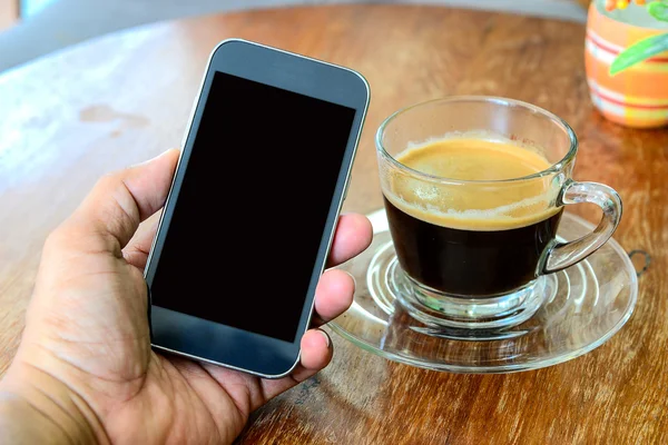 Smart mobiltelefon i handen, kaffe på träbord. — Stockfoto