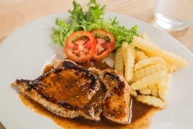 Beyaz tabak, bardak su, patates kızartması ahşap üzerinde domuz eti biftek 