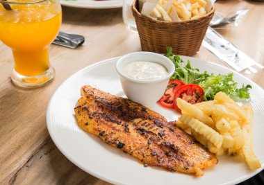 Balık biftek beyaz tabak, bardak su, patates kızartması, turuncu jui içinde