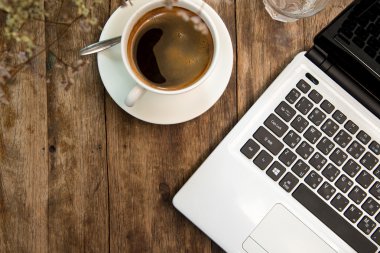 Beyaz kahve fincanı ve ahşap masa üstünde laptop.