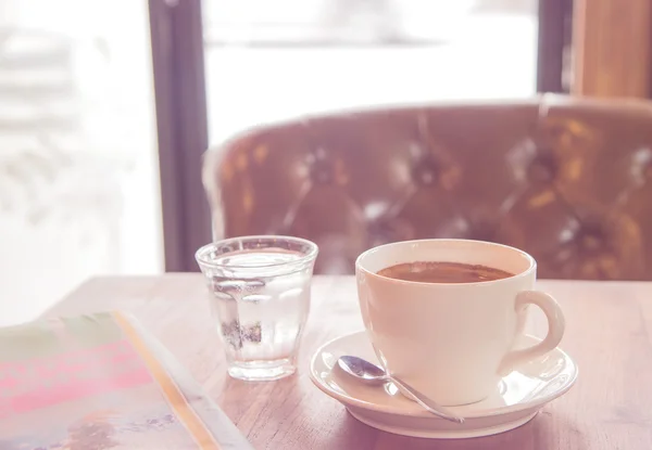 White coffee cup, blurred newspaper and glass water on wooden ta — стоковое фото