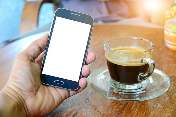 Smart phone in hand with coffee on wooden table.
