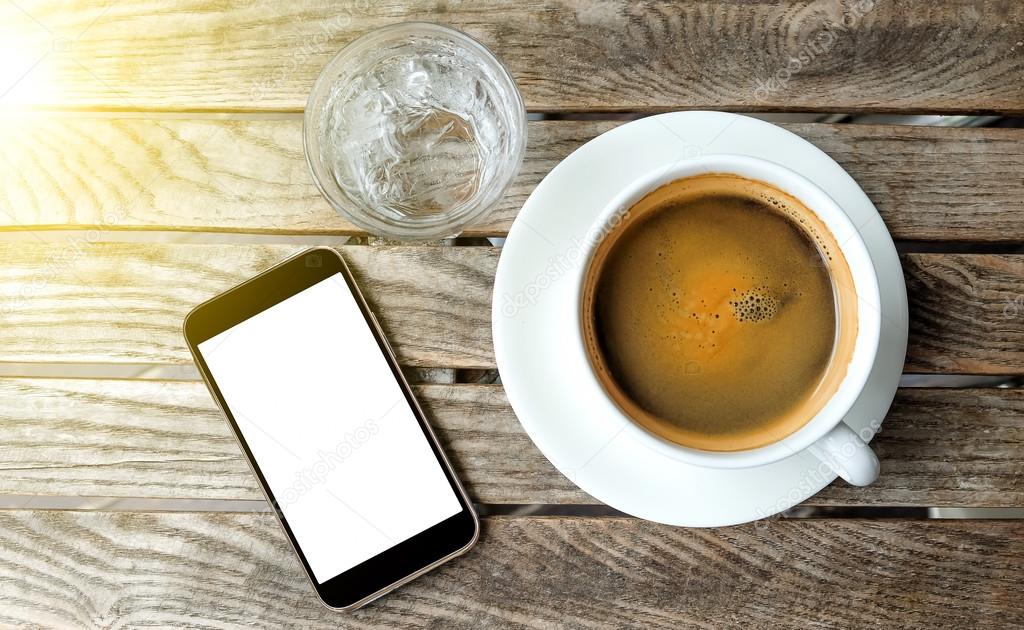 White coffee cup and glass water with smart phone on wooden tabl