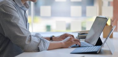 Modern bir ofiste dizüstü bilgisayar ve dijital tablet kullanan bir adamın görüntüsü..