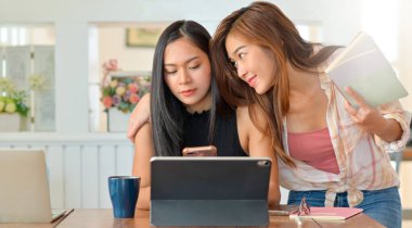 İki genç kadın okurken ve akıllı telefon kullanırken birbirleriyle dalga geçiyorlar..