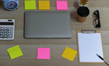 Boş bir klip tahtası ve ofis malzemeleriyle birlikte hesap makinesi olan laptop, masadaki kahve fincanını kaldır. Üst görünüm ofis masası..