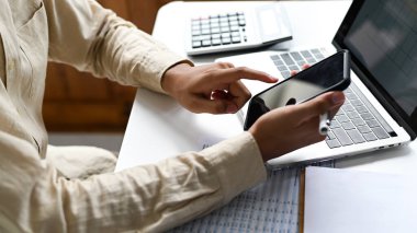 El bilgisayarlı bir akıllı telefon kullanıyor ve masanın üzerine grafikler koyuyor, iş masası..