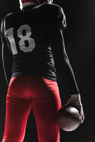 American football speler poseren met bal op zwarte achtergrond — Stockfoto