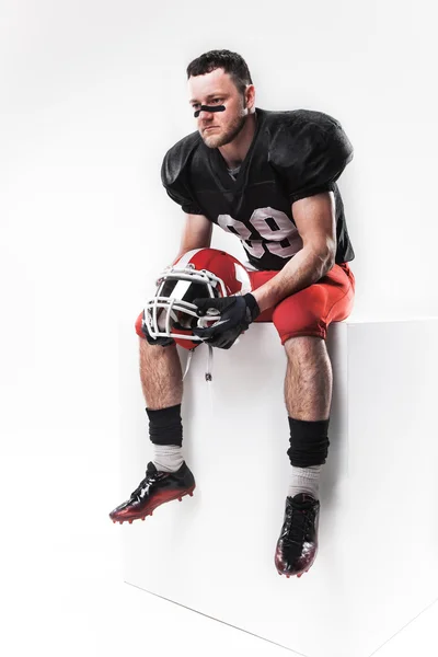 American football speler zitten met helm op witte achtergrond — Stockfoto
