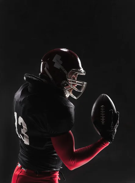 Jogador de futebol americano posando com bola no fundo preto — Fotografia de Stock