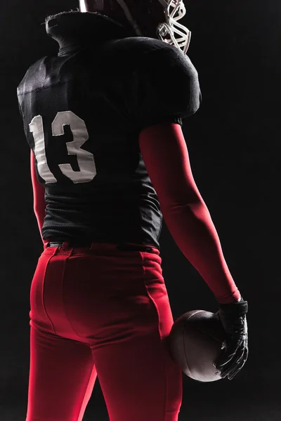 Americký fotbalista pózuje s míčem na černém pozadí — Stock fotografie