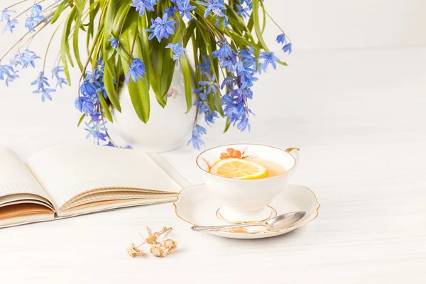Чай з лимоном і букетом блакитних первоцвітів на столі — стокове фото
