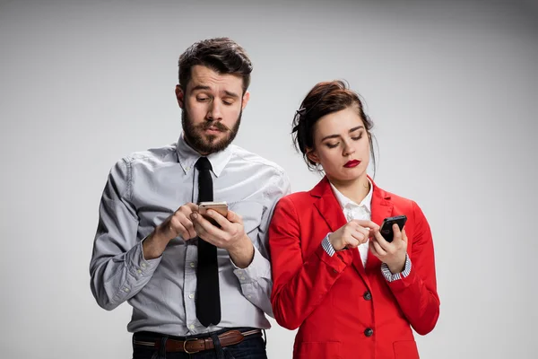 Concepto de negocio. Los dos jóvenes colegas sosteniendo teléfonos móviles sobre fondo gris — Foto de Stock
