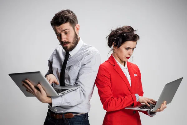The young businessman and businesswoman with laptops  communicating on gray background — Stock Photo, Image