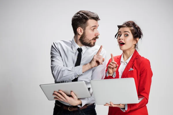 O jovem empresário e empresária com laptops se comunicando em fundo cinza — Fotografia de Stock