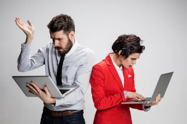 El joven hombre de negocios y mujer de negocios con ordenadores portátiles que se comunican sobre fondo gris — Foto de Stock