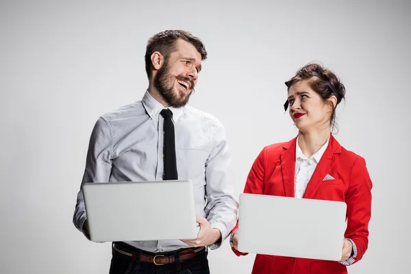 Il giovane uomo d'affari e donna d'affari con computer portatili che comunicano su sfondo grigio — Foto Stock