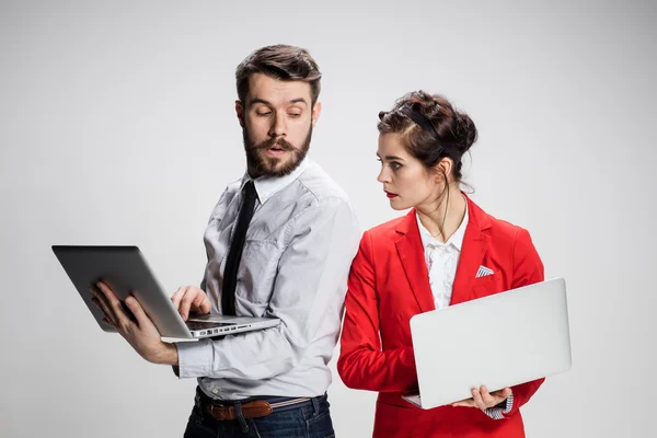 Il giovane uomo d'affari e donna d'affari con computer portatili che comunicano su sfondo grigio — Foto Stock