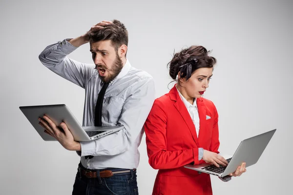 El joven hombre de negocios y mujer de negocios con ordenadores portátiles que se comunican sobre fondo gris —  Fotos de Stock
