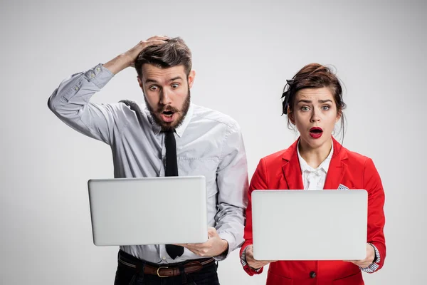 Den ung affärsman och affärskvinna med bärbara datorer kommunicerar på grå bakgrund — Stockfoto