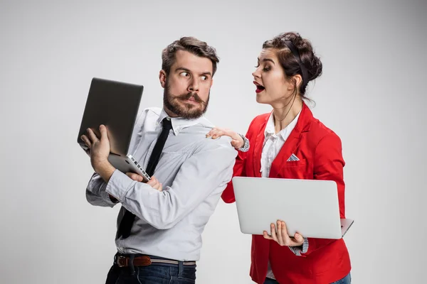 Le jeune homme d'affaires et femme d'affaires avec des ordinateurs portables communiquant sur fond gris — Photo
