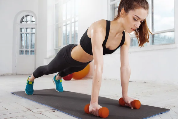 Vacker smal brunett gör några armhävningar en gymmet — Stockfoto