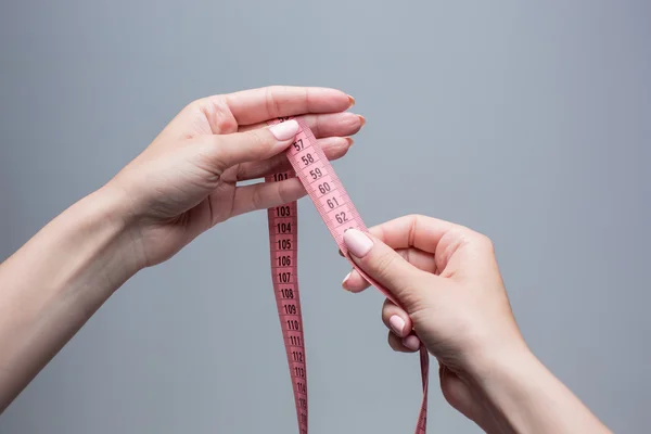 The tape in female hands on gray background. Weight loss, diet