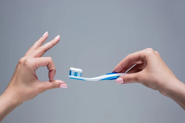 Cepillo de dientes en las manos de las mujeres en gris — Foto de Stock