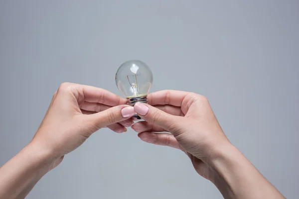 Manos sosteniendo una bombilla incandescente sobre fondo gris — Foto de Stock