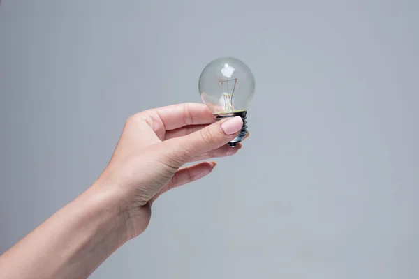 Mano sosteniendo una bombilla incandescente sobre fondo gris — Foto de Stock