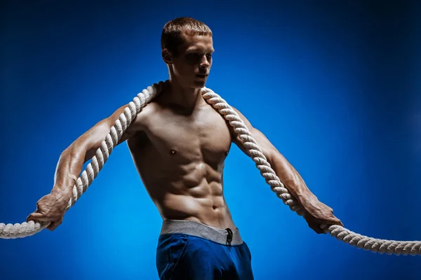 Ajuste o jovem com belo tronco e uma corda no fundo azul — Fotografia de Stock