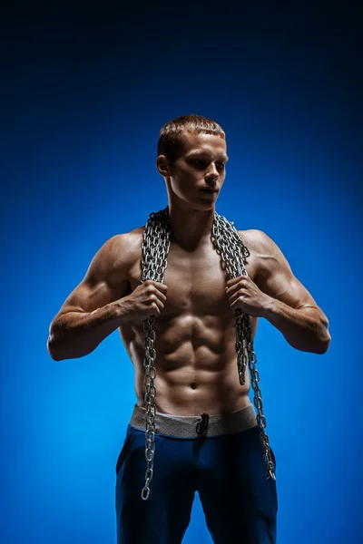 Tipo musculoso con cadenas en los hombros contra una pared azul — Foto de Stock