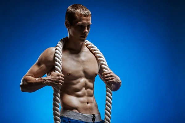 Ajuste o jovem com belo tronco e uma corda no fundo azul — Fotografia de Stock