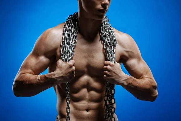 Tipo musculoso con cadenas en los hombros contra una pared azul —  Fotos de Stock