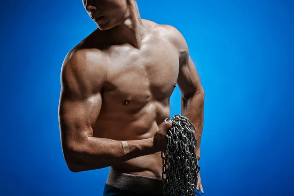 Muskulöser Typ mit Ketten an den Schultern vor einer blauen Wand — Stockfoto
