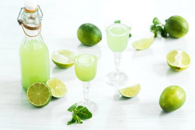 Beyaz ahşap arka plan üzerinde bir bardak ve taze limon ve limon ev kireç likörü