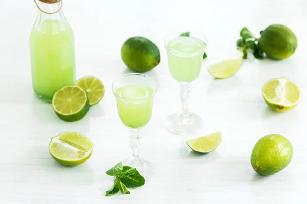 Likier wapienno-domowy w szklance i świeżych cytrynie, Limes na białym tle drewnianym — Zdjęcie stockowe