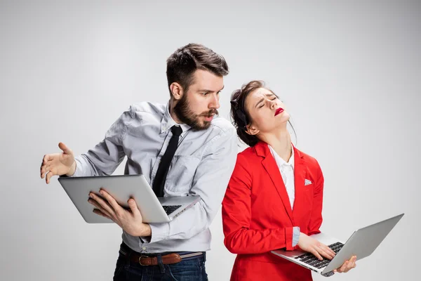Le jeune homme d'affaires et femme d'affaires avec des ordinateurs portables sur fond gris — Photo